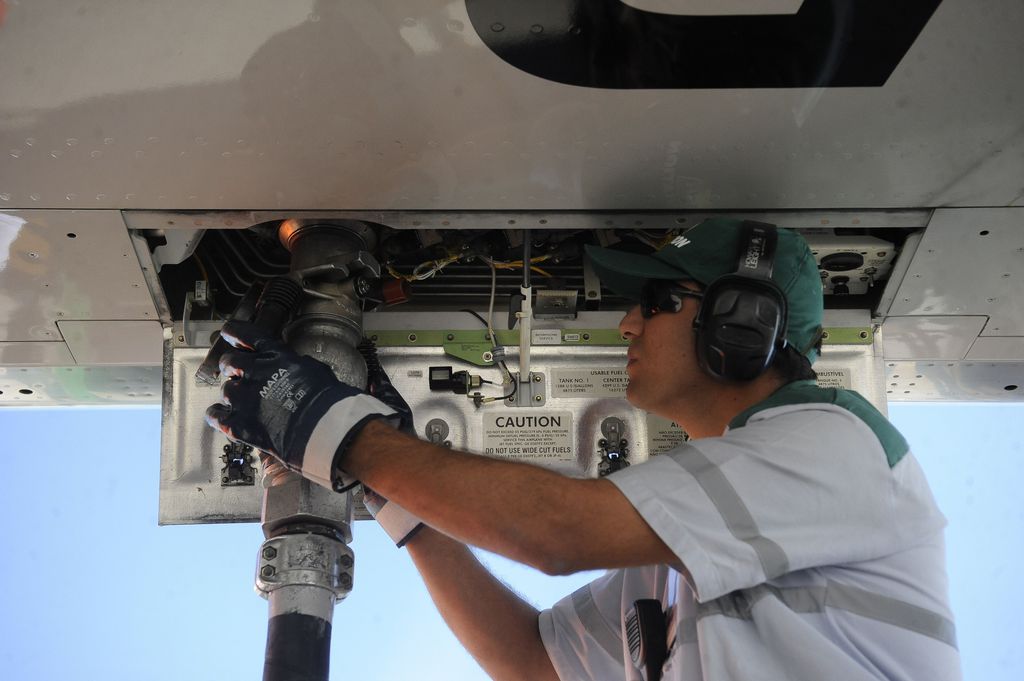 Na imagem: Homem branco conecta, à parte de baixo de aeronave, mangueira para abastecimento de aeronave com SAF, biocombustível de aviação (Foto: Tânia Rêgo/Agência Brasil)