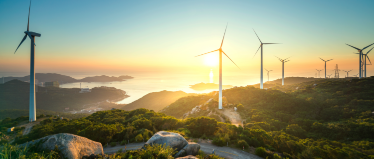 Inflação eleva margens para renováveis em 2022, indica relatório da Platts. Na imagem: Turbinas eólicas sobre montanhas cobertas com vegetação e, ao fundo, sol brilhando se reflete no oceano (Foto: Reprodução Twitter EY)