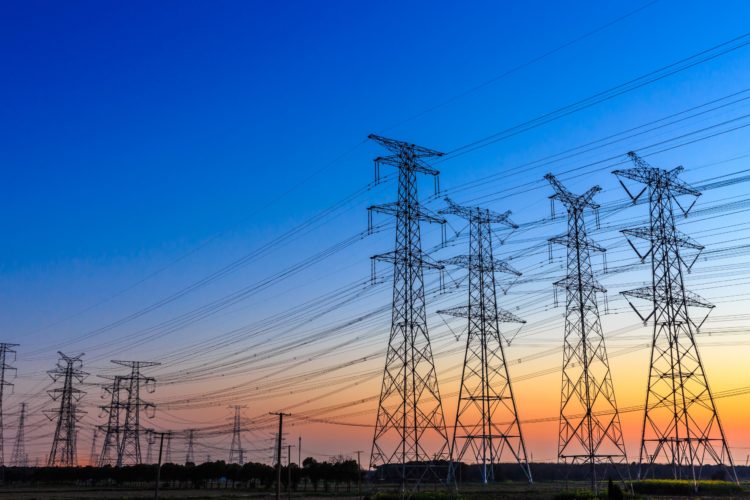 Consumo de energia elétrica cresce 4,1% em 2021, aponta CCEE. Na imagem: Foto à contraluz de grandes torres com linhas de transmissão de energia ,sob céu azul com pôr do sol ao fundo (Foto: iStock)