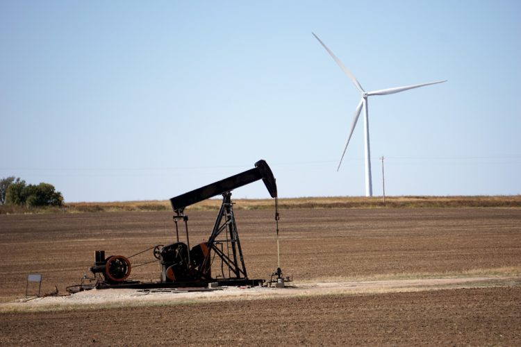 Transição energética vai custar US$ 5,7 trilhões por ano até 2030. Na imagem: Bomba de petróleo para exploração onshore em um terreno descampado, com turbinas eólicas ao fundo (Foto: Michael/Pixabay)