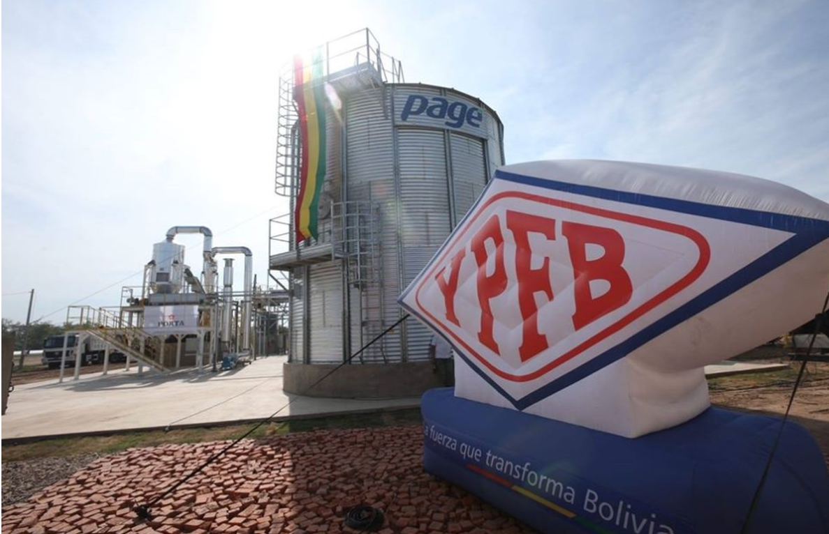 YPFB fecha acordo com Petrobras e melhora preços do gás boliviano. Na imagem: Placa escrita YPFB e tanque de armazenamento na cor prata com faixa pendurada nas cores da bandeira da Bolívia: vermelho, amarelo e verde (Foto: Divulgação YPFB)