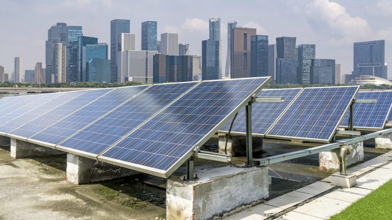 Placas solares fotovoltaicas sobre terraço, em primeiro plano, e, ao fundo, grande quantidade de prédios altos, em centro urbano. GD solar (Foto: Divulgação/Acenty)