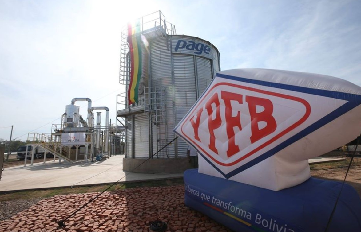 Bolívia quer diversificar clientes de gás natural no Brasil. Na imagem: Placa escrita YPFB e tanque de armazenamento na cor prata com faixa pendurada nas cores da bandeira da Bolívia: vermelho, amarelo e verde (Foto: Divulgação YPFB)