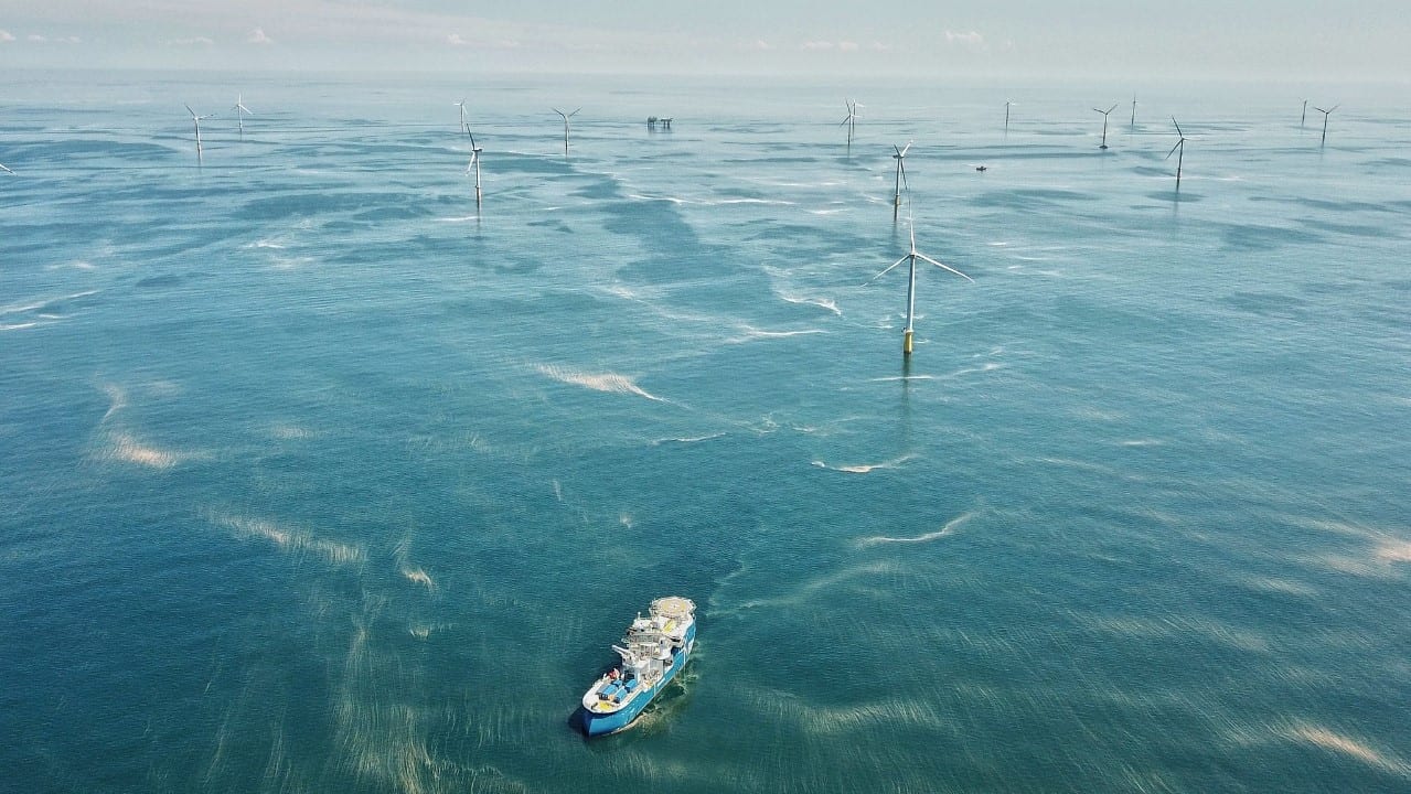 Capacidade eólica offshore crescerá sete vezes até 2032, prevê Woodmac. Na imagem: Embarcação próxima a turbinas eólicas offshore, em mar azul com pequenas ondas pelo vento (Foto: GWEC)