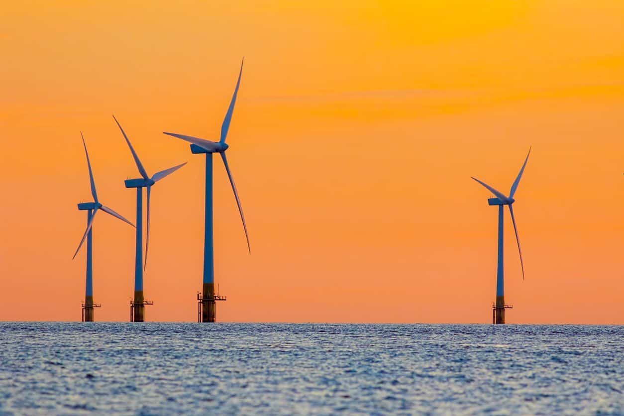 Turbinas eólicas offshore em mar azul acinzentado e céu alaranjado (Foto: Pixabay)
