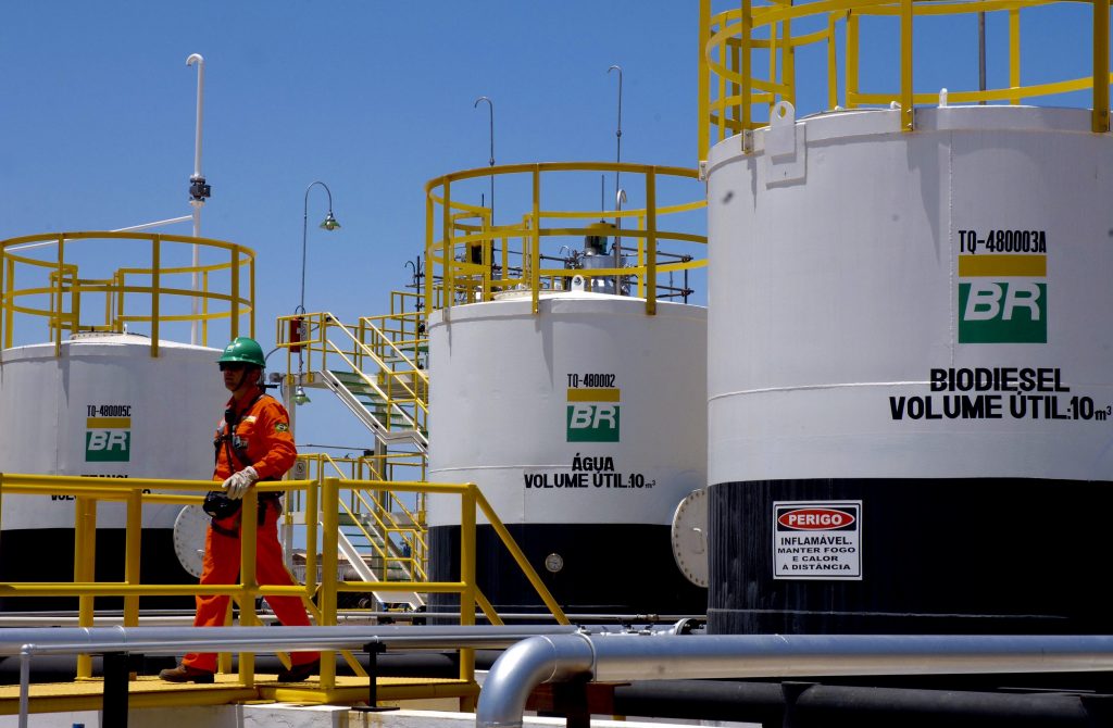 Petrobras Biocombustível registra aumento de 35% na comercialização de biodiesel. Na imagem: Trabalhadores de uniforme laranja passam em frente a tanques de armazenamento de combustíveis em planta da PBIO – Petrobras Biocombustível (Foto: Divulgação PBIO)