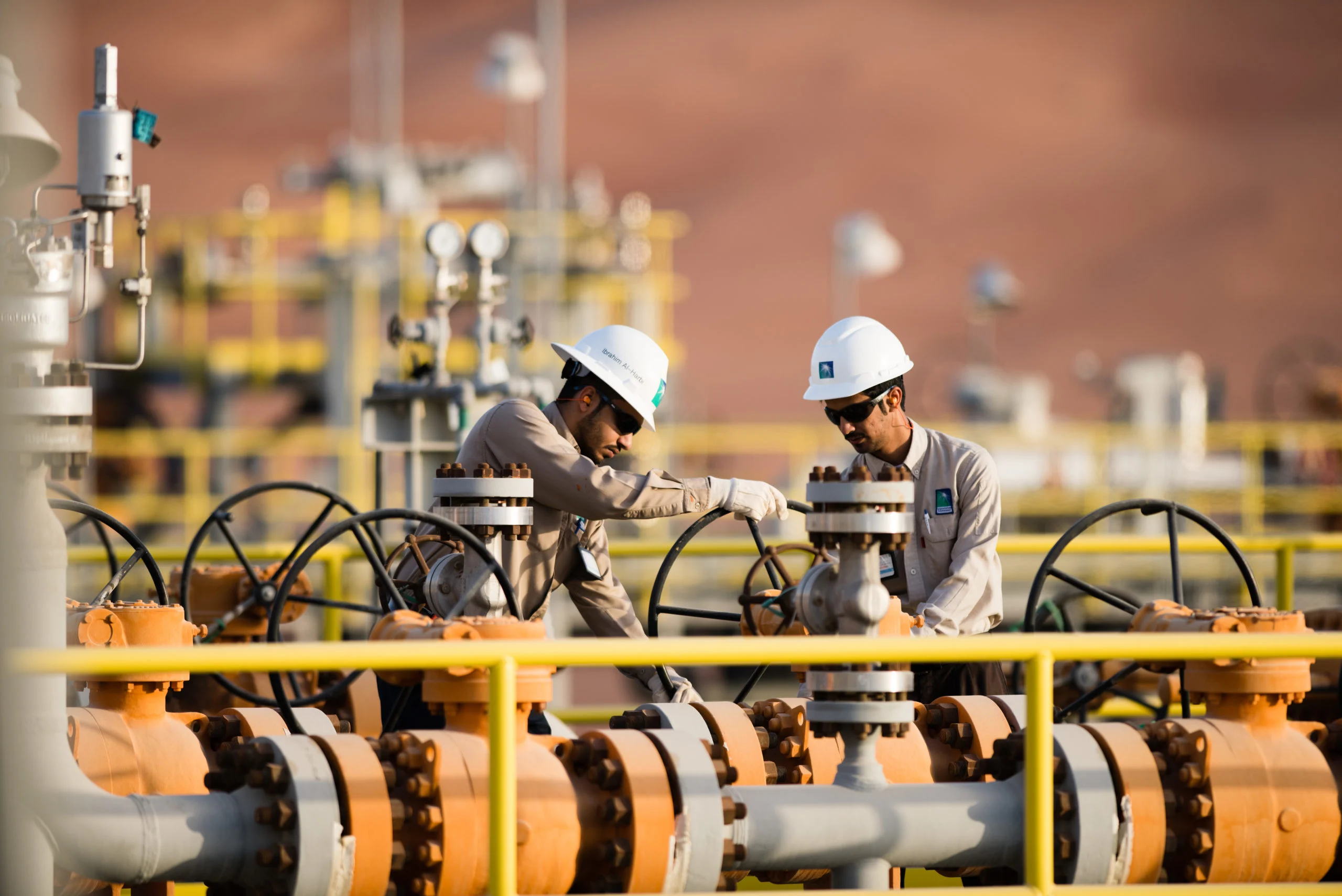 Preço do petróleo ainda resiste à pressão da Opep. Na imagem: Dois trabalhadores, com uniformes cinza e capacete de proteção branco, operam instalações em gasoduto (Foto: Divulgação/Saudi Aramco)