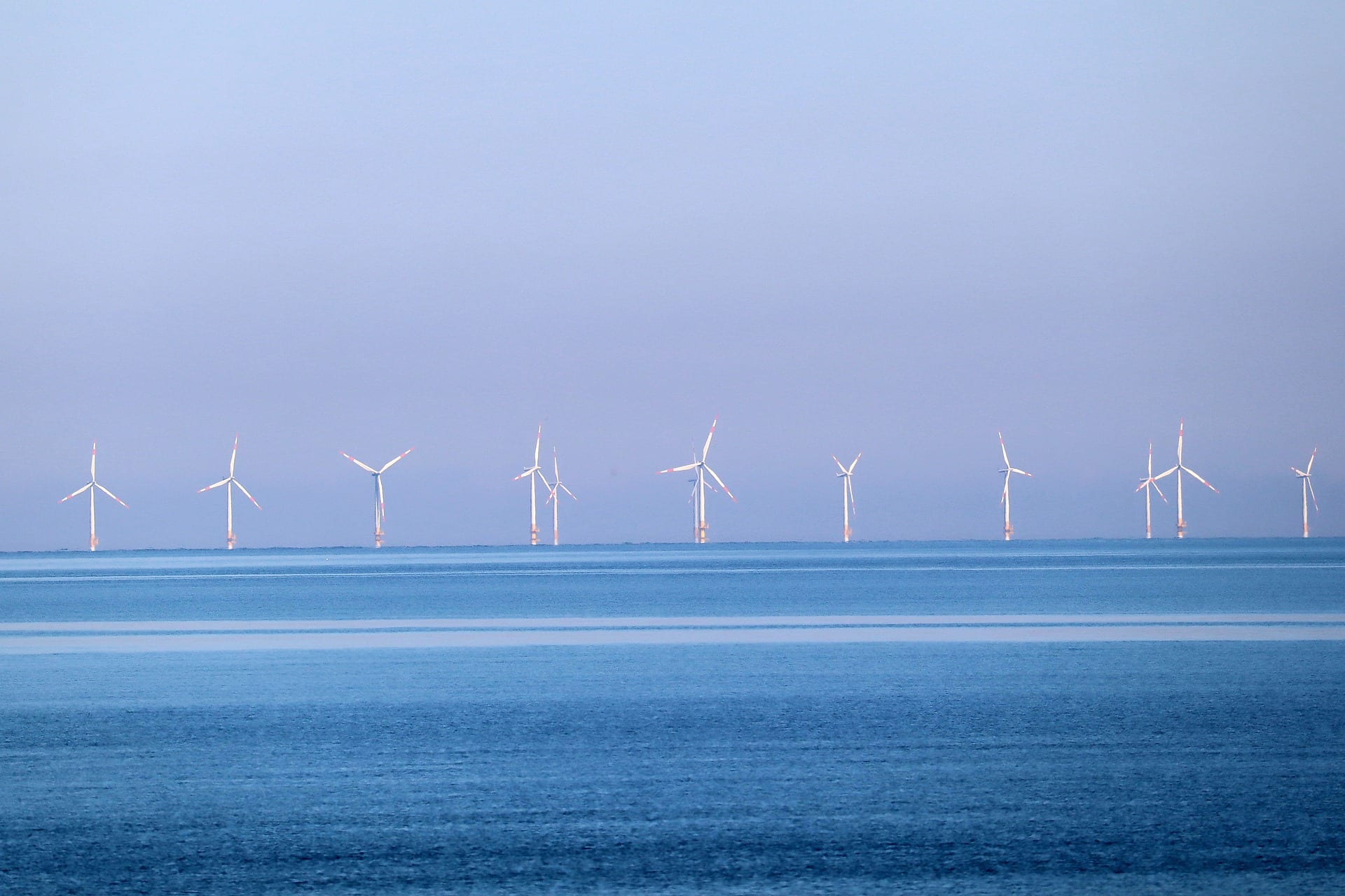 Colômbia prevê leilão para eólicas offshore, mas sem avaliar impactos ambientais. Na imagem: Praia com mar azul e, ao fundo, aerogeradores de parque eólico offshore (Foto: Thomas G./Pixabay)