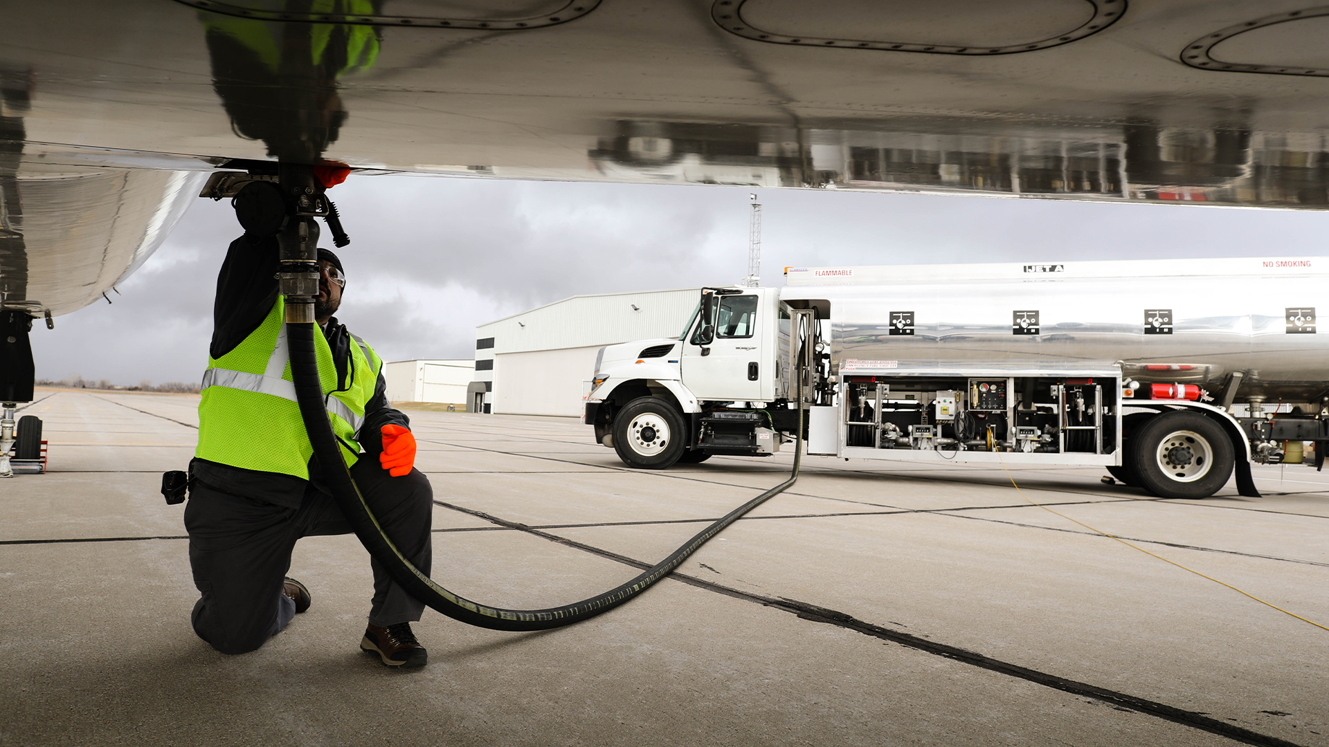 Os combustíveis sustentáveis de aviação (SAF) e o Corsia, o programa de descarbonização de voos internacionais. Na imagem: Trabalhador conecta mangueira de caminhão tanque à compartimento na parte de baixo da asa de aeronave para abastecimento (Foto: EiDA)