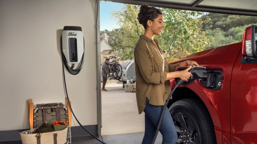 Montadoras BMW, Ford e Honda criam join venture ChargeScape para integrar veículos à rede elétrica. Na imagem: Mulher branca segura plug para conectar veículo elétrico vinho à rede de energia (Foto: Divulgação Ford)