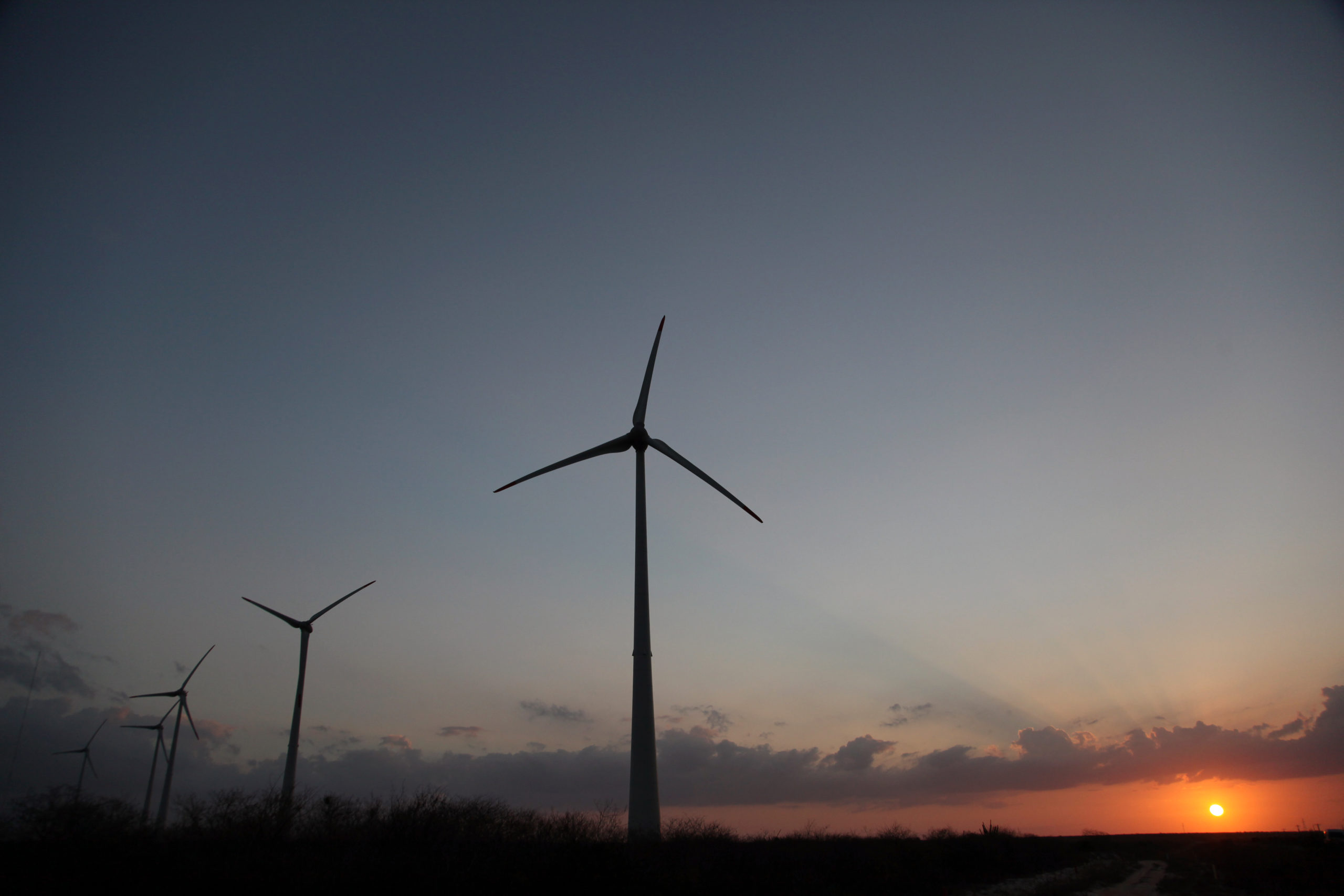 Petrobras e WEG fazem parceria para desenvolver turbina eólica. Na imagem: Turbinas eólicas fotografadas ao anoitecer, à contraluz, com sol se pondo ao fundo (Foto: Divulgação Petrobras)
