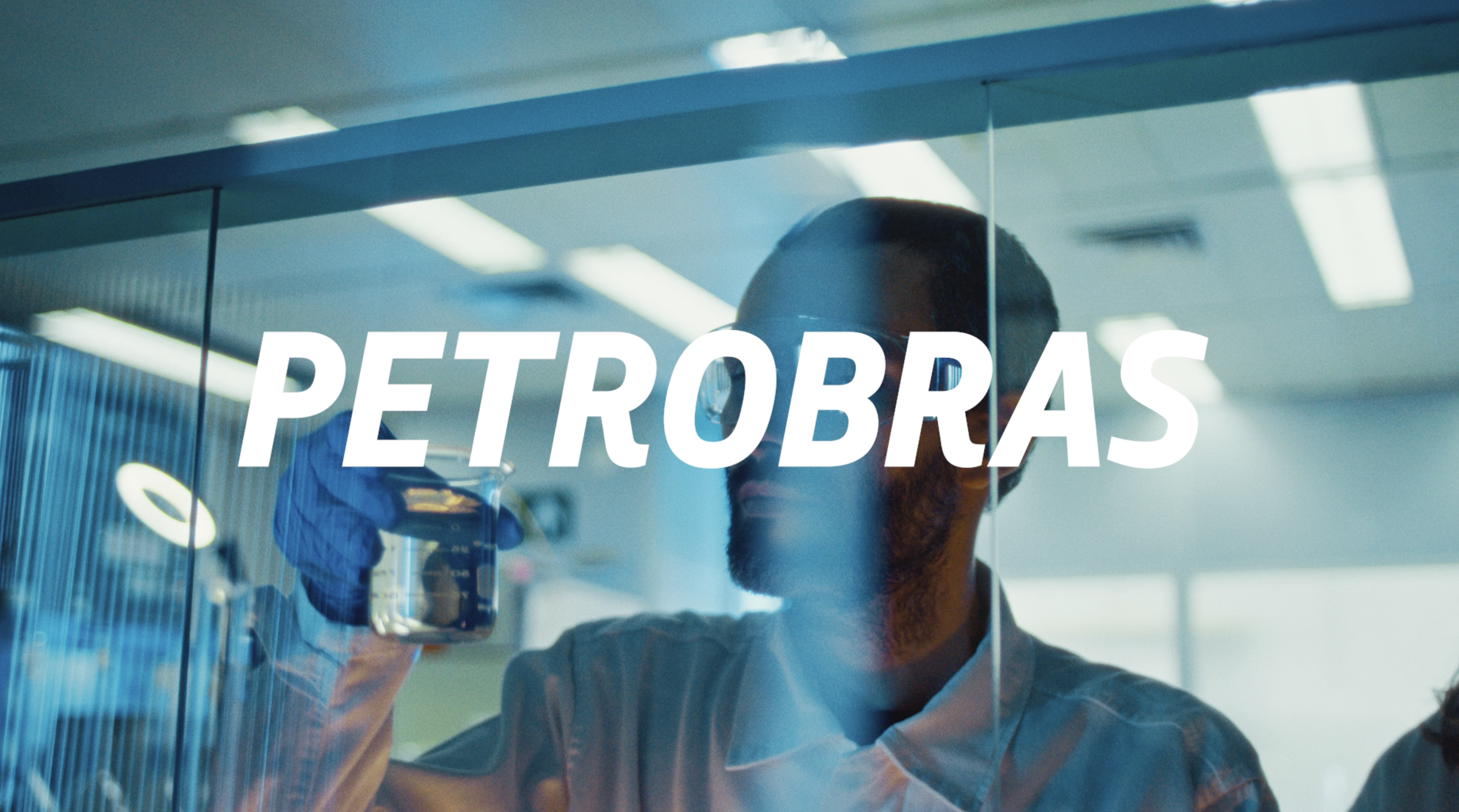 Petrobras compensará emissões de gasolina Podium com créditos de carbono, o primeiro combustível carbono neutro do Brasil. Na imagem: Homem negro, atrás de uma parede de vidro, analisa gasolina Podium em frasco de vidro em laboratório da Petrobras (Foto: Agência Petrobras)