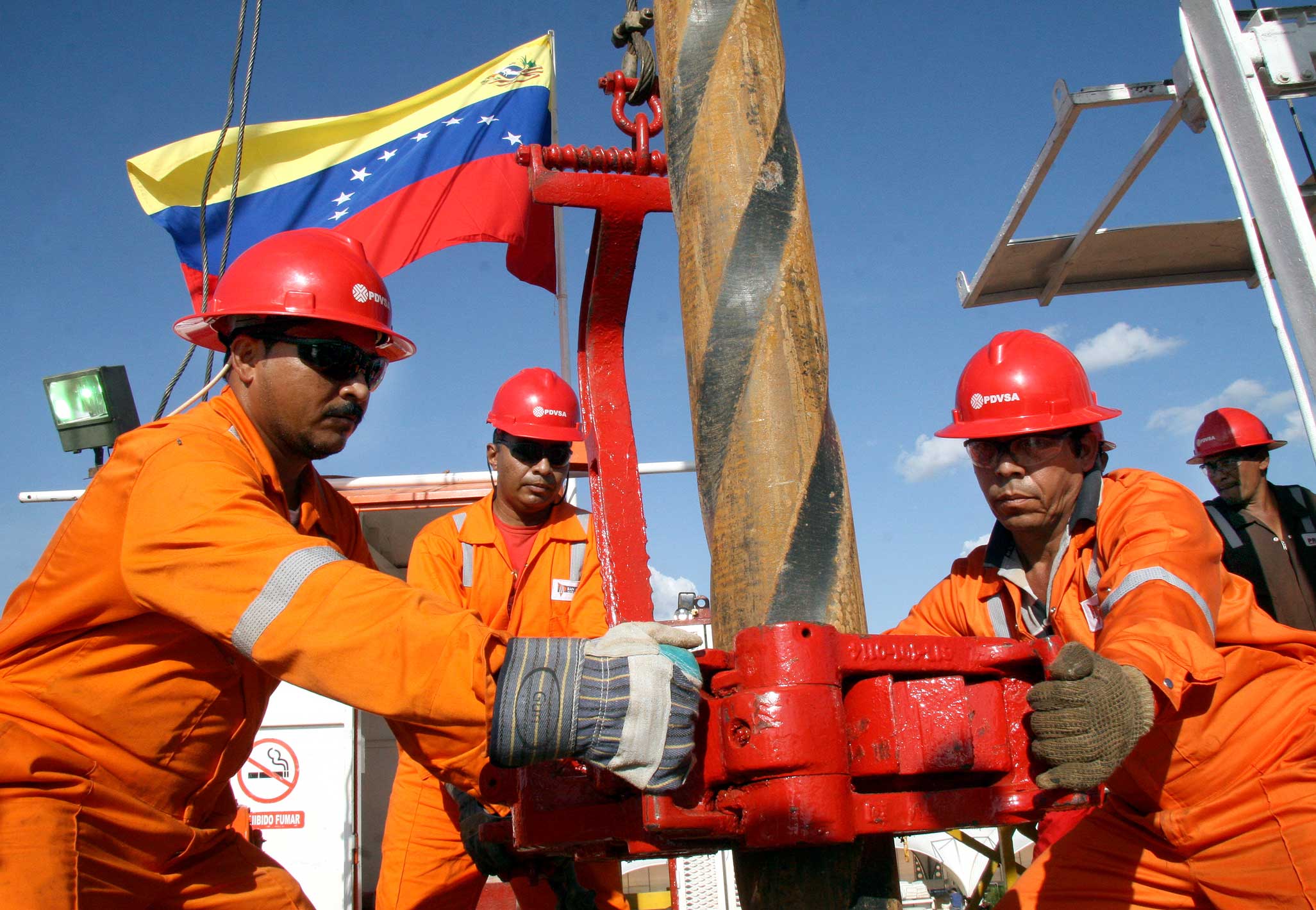 Recuperação da indústria petrolífera na Venezuela é improvável no curto prazo, afirmam especialistas do O&G. Na imagem: Funcionários da PDVSA, petroleira estatal da Venezuela, operam equipamento de perfuração; uniformizados, em laranja, com equipamentos e sinalizações de segurança e capacete vermelho (Foto: Divulgação)