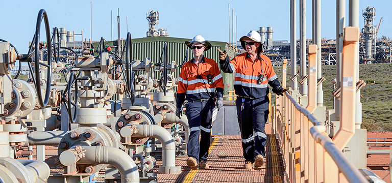 Como a greve em plantas da Chevron, na Austrália, afeta o mercado global de GNL e o Brasil. Na imagem: Dois trabalhadores brancos, uniformizados e com chapéus e óculos escuros caminham e inspecionam instalações da planta de GNL Gorgon, da Chevron, na Austrália (Foto: Divulgação Chevron)