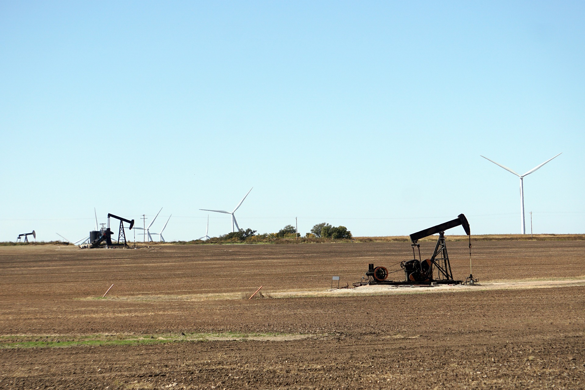 Receitas de países dependentes de petróleo podem ter queda pela metade em cenário de transição energética acelerada, diz Carbon Tracker Initiative. Na imagem: Cavalos-de-pau para a produção onshore de petróleo, em Oklahoma (EUA), com turbinas eólicas ao fundo (Foto: Mike/RJA1988/Pixabay)