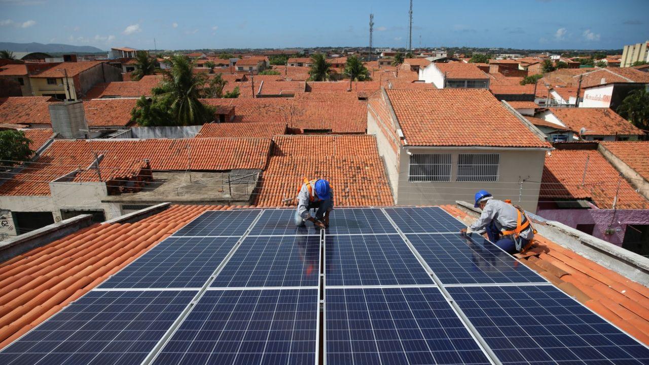 Geração própria em sistemas de micro e minigeração de energia solar cresce 40% em 2023 no Brasil. Na imagem: Dois trabalhadores instalam placas fotovoltaicas sobre telhado para geração solar (Foto: Natinho Rodrigues)