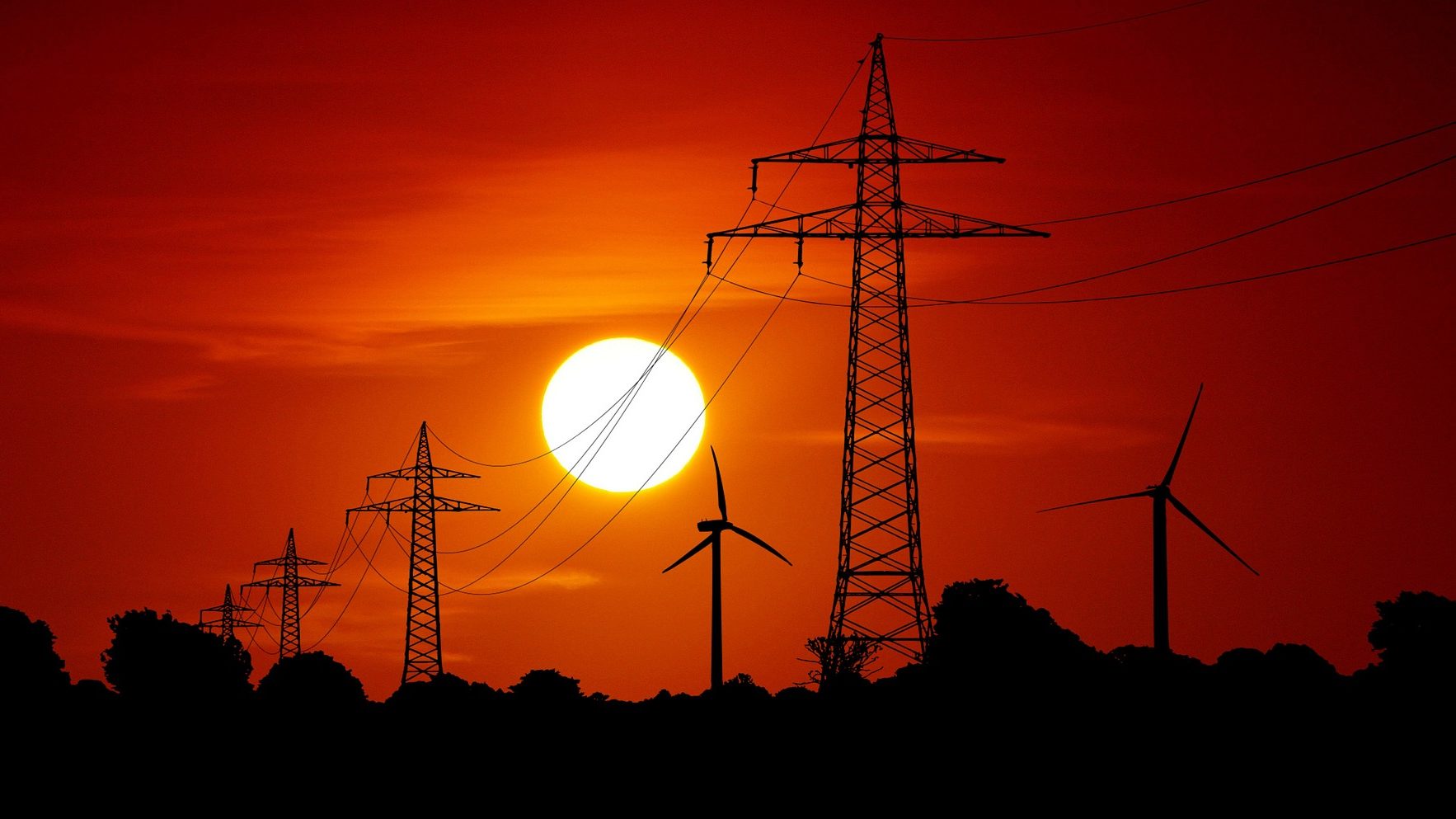 Torres e linhas de transmissão de energia com turbinas eólicas ao fundo e, no horizonte, o sol se põe (Foto: Peter Schmidt/Terranaut/Pixabay)